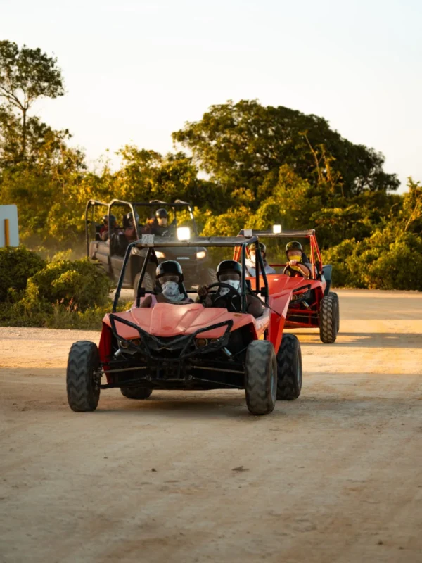Two riders in helmets sit in red off-road buggies on a sandy track in evening light