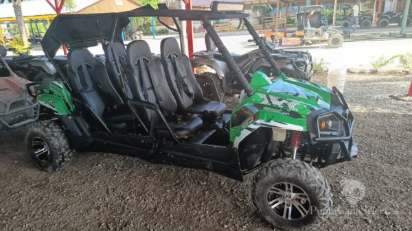 A green four-seat buggy parked on gravel with more vehicles lined up behind