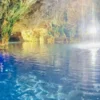 Daylight falls through the mouth of a cave onto the still blue water of a cenote