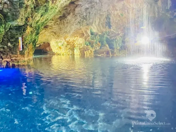 Daylight falls through the mouth of a cave onto the still blue water of a cenote