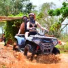Two riders on a quad bike cross an orange mud puddle as other guests wait behind