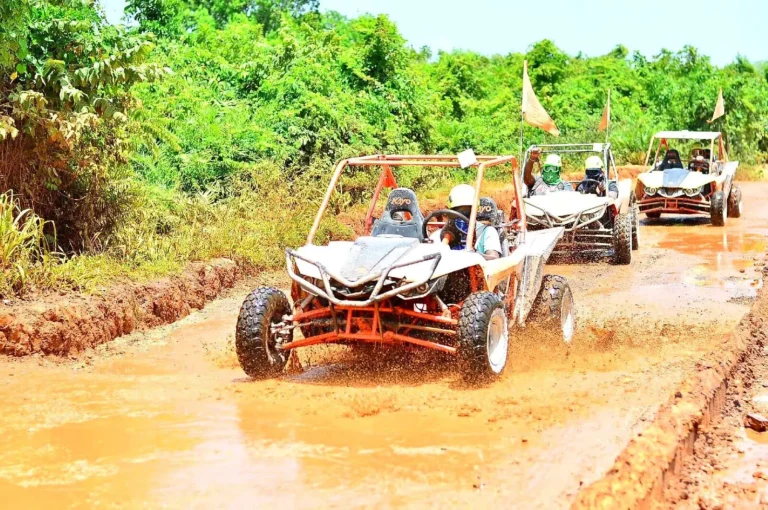 A convoy of off-road buggies splashes through a muddy jungle track, the lead pair throwing up spray