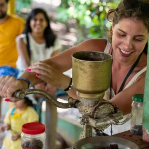A guest turning a hand-cranked mill to grind roasted cacao at a Dominican countryside home, with ground cacao on a plate beside her