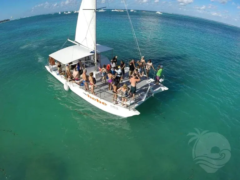 Guests fill the deck of a catamaran under sail on clear turquoise water