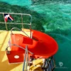 A red water slide mounted on the deck of a catamaran, with a Dominican flag flying beside it