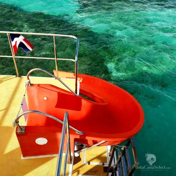 A red water slide mounted on the deck of a catamaran, with a Dominican flag flying beside it