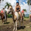 Horseback riding at the ranch A guest on horseback smiling under royal palms with the Anamuya hills behind