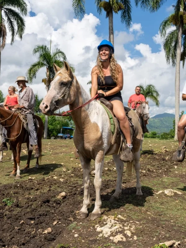 Horseback riding at the ranch A guest on horseback smiling under royal palms with the Anamuya hills behind