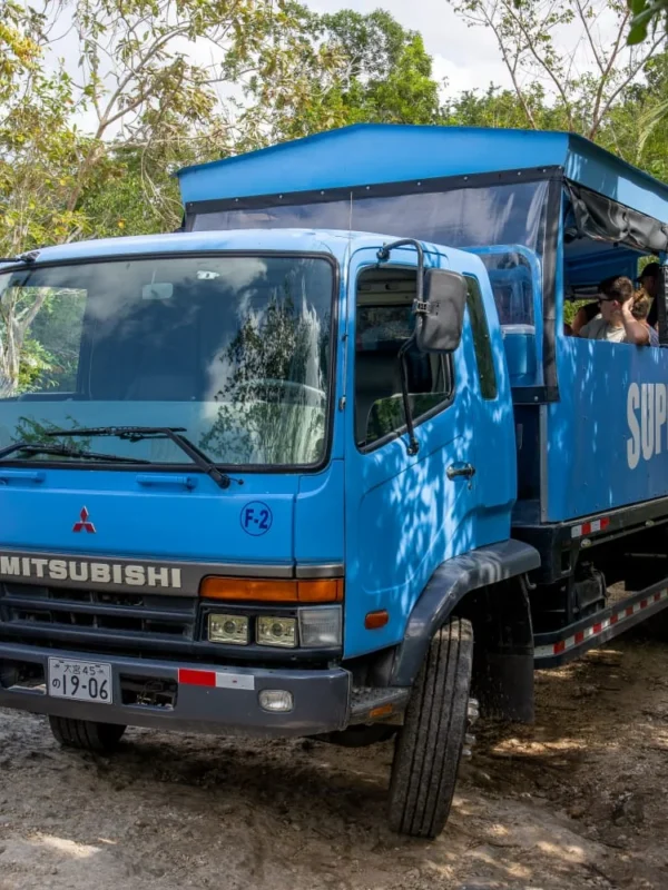 Open safari truck on the countryside route An open safari truck carrying guests along a dirt road through dense green countryside