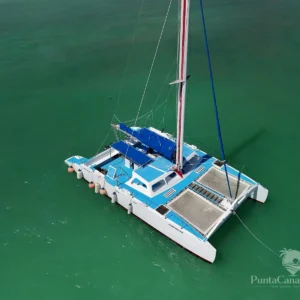 A blue and white catamaran lies at anchor on calm green water, seen from above