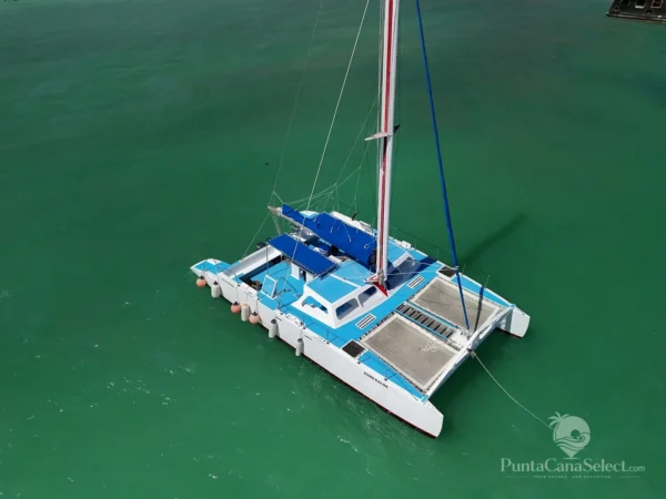 A blue and white catamaran lies at anchor on calm green water, seen from above