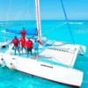 Five crew in red shirts stand on the bow netting of the catamaran Esmeralda