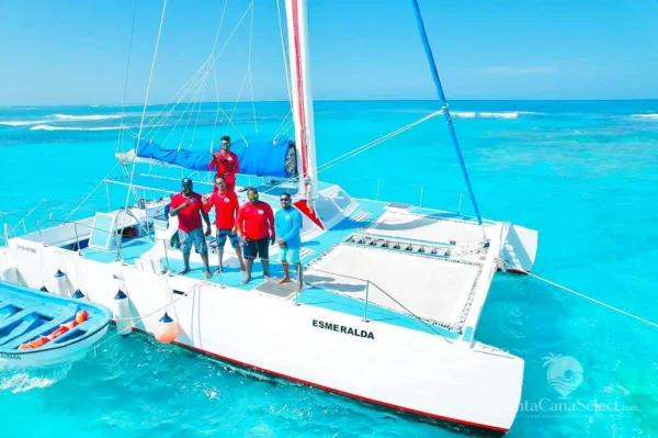 Five crew in red shirts stand on the bow netting of the catamaran Esmeralda