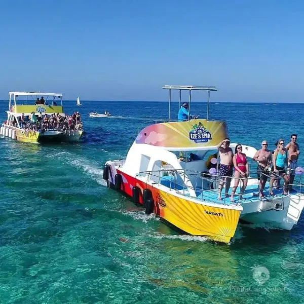 Guests line the rail of a yellow party boat as a second crowded boat follows across open water