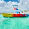 A rainbow-painted party catamaran sits in shallow turquoise water off a resort shoreline