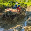 A buggy splashes through a muddy rut with spray flying from the front wheels