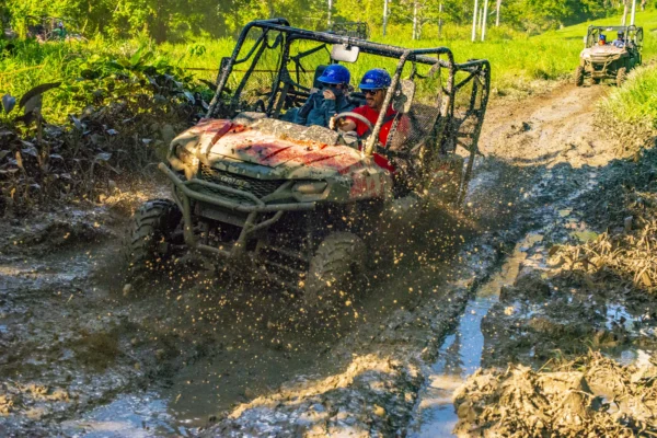 A buggy splashes through a muddy rut with spray flying from the front wheels