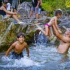 A father lifts a small child above the water while a boy splashes nearby at the river stop