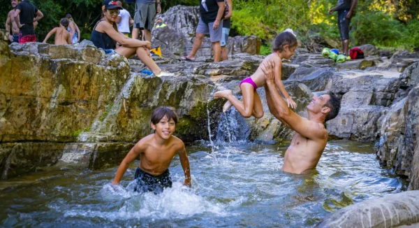 A father lifts a small child above the water while a boy splashes nearby at the river stop