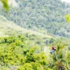 A zipline rider crosses high above a broad forested valley