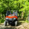 A red four-seater buggy drives head-on along a shaded jungle trail