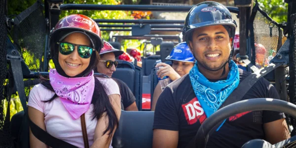 A couple in helmets and bandanas smile from the front seats of a buggy