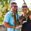A couple laugh as squirrel monkeys climb across them with green hills behind