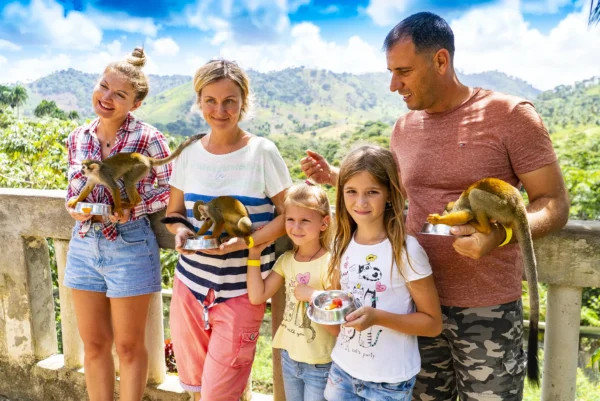 A family of five stands at a viewpoint rail with squirrel monkeys perched on their arms