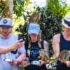 Three guests laugh as squirrel monkeys perch on their caps while they hold feeding bowls