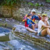 A family sits together on flat rocks beside the Anamuya River at the swim stop