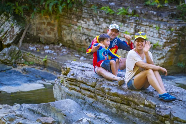 A family sits together on flat rocks beside the Anamuya River at the swim stop