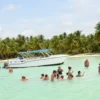 Guests swimming beside the anchored boat at Saona Island Guests stand and swim in waist-deep turquoise shallows beside the anchored La Cherna speedboat, with Saona Island's palm-lined beach behind