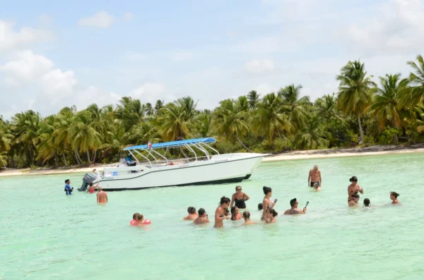 Guests swimming beside the anchored boat at Saona Island Guests stand and swim in waist-deep turquoise shallows beside the anchored La Cherna speedboat, with Saona Island's palm-lined beach behind
