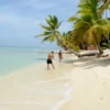Couple walking the Saona Island shoreline A couple walks along the water's edge on Saona Island's white sand beach beneath leaning coconut palms