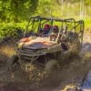 A mud-covered buggy drives through a deep rutted puddle in open country