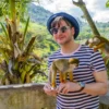A guest in a striped shirt holds a feeding cup while two squirrel monkeys climb his arm and shoulder