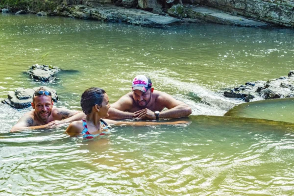 Three guests stand chest-deep in the Anamuya River laughing together