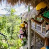 Child launching from the zipline platform with a guide A child in a yellow helmet sets off along a zipline as a guide steadies the cable from the platform