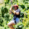Rider mid-line on the Punta Cana zipline course A woman in a red helmet and safety harness laughs while riding a zipline high above the treetops