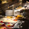 A buffet line of Dominican dishes with a guest lifting a plate of rice, stewed meat and fresh fruit