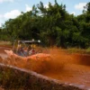 A dune buggy throws up a wall of red mud as it powers through a flooded jungle trail