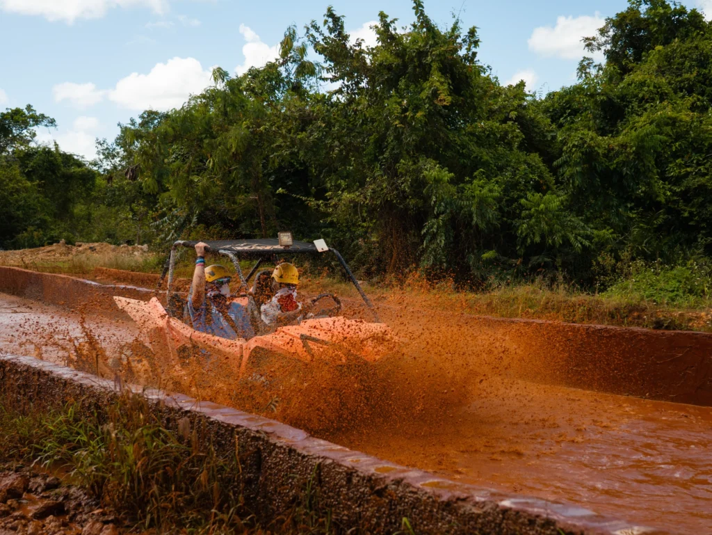 A dune buggy throws up a wall of red mud as it powers through a flooded jungle trail