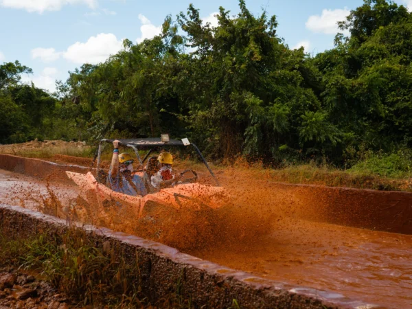 A dune buggy throws up a wall of red mud as it powers through a flooded jungle trail
