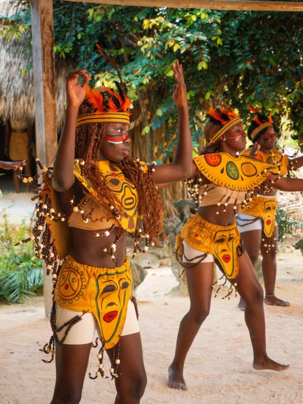Dancers in feathered headdresses and painted body art perform an ancestral dance in the Taíno village clearing