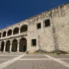 The stone facade of the Alcazar de Colon rising over the empty paving of Plaza Espana under a deep blue sky