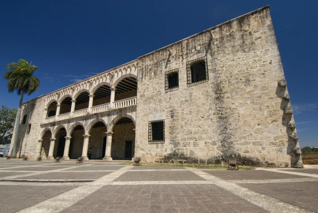 The stone facade of the Alcazar de Colon rising over the empty paving of Plaza Espana under a deep blue sky